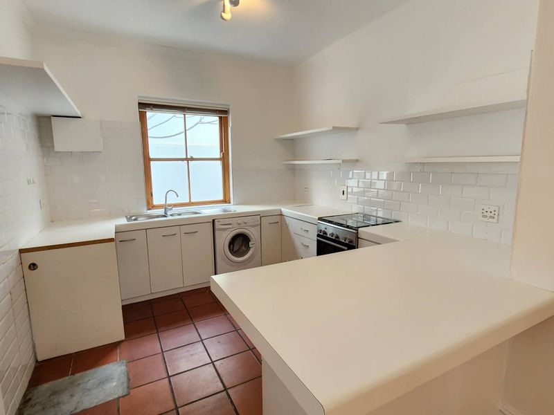 A functional kitchen featuring white cabinetry, subway tile backsplash, terracotta flooring, and a breakfast bar, offering a clean and bright workspace.