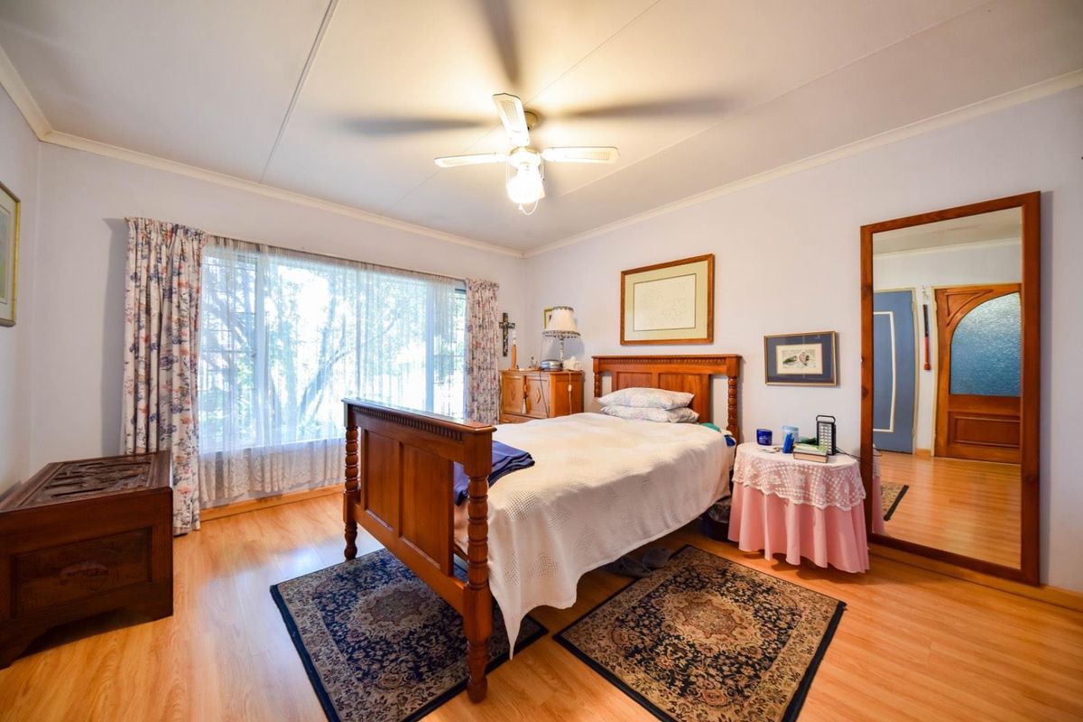 A well-lit bedroom featuring laminate flooring, a ceiling fan, and a large window providing natural light.