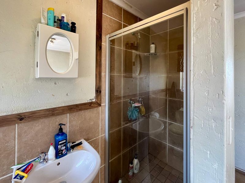A dated bathroom featuring a tiled shower enclosure, a wall-mounted basin, and a small medicine cabinet.