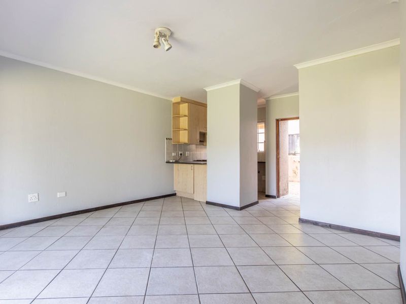 An open-plan living area featuring neutral tiled flooring, a compact kitchen corner with built-in cabinetry, and direct access to an exterior doorway.