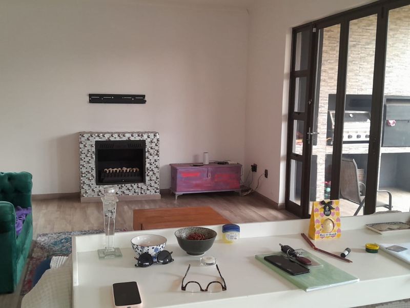 Open plan living area featuring laminate flooring, a built-in fireplace with mosaic tiling, and bi-fold doors leading to an outdoor braai area.