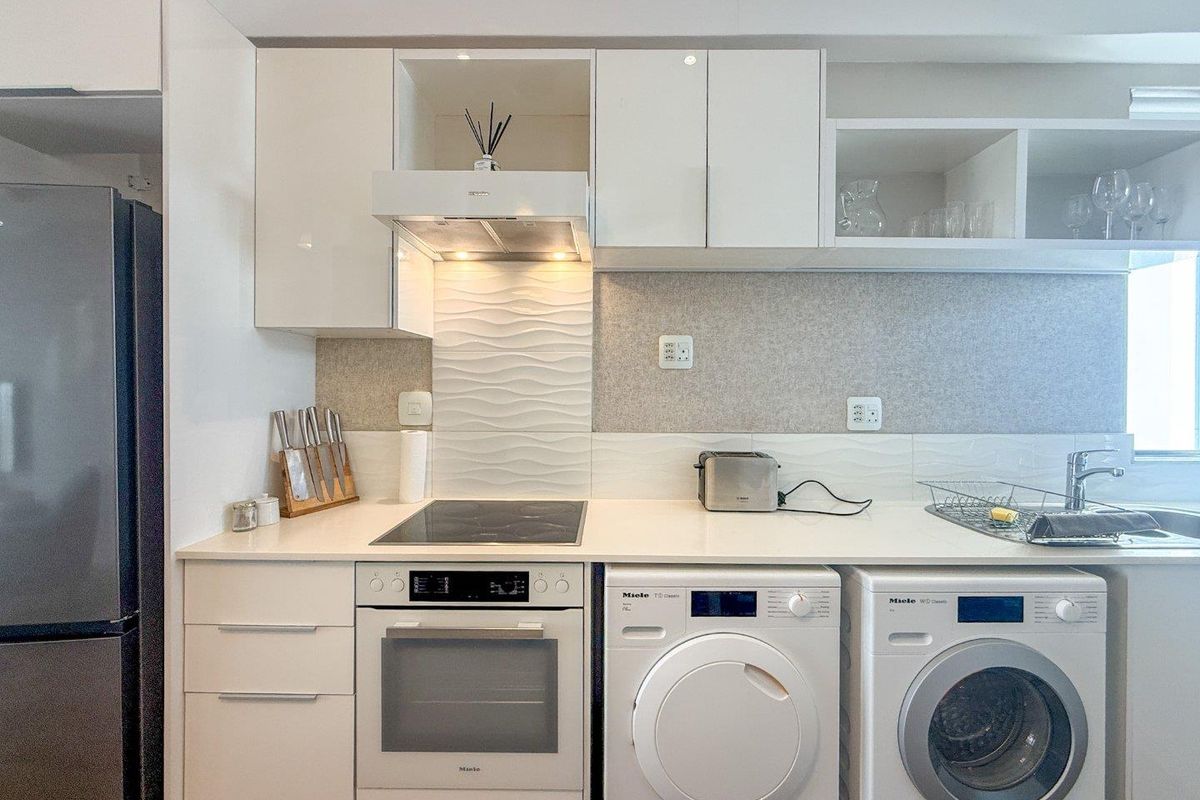Modern kitchen featuring white high-gloss cabinetry, quartz countertops, textured splashback, integrated oven, hob, extractor fan, and built-in laundry appliances.