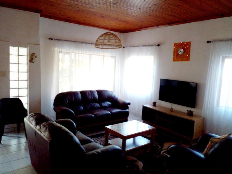 A comfortable living room featuring a warm timber-clad ceiling, tiled flooring, and a unique glass block feature wall, providing a cozy and inviting atmosphere.