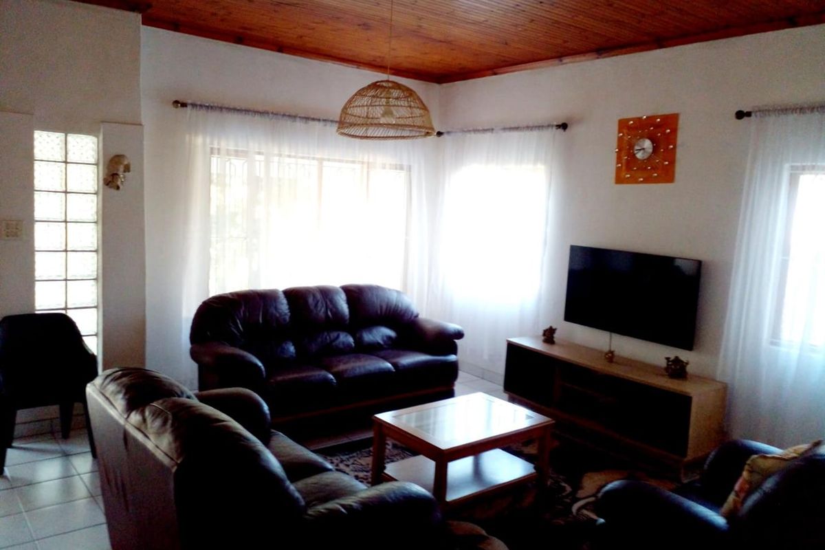 A comfortable living room featuring a warm timber-clad ceiling, tiled flooring, and a unique glass block feature wall, providing a cozy and inviting atmosphere.
