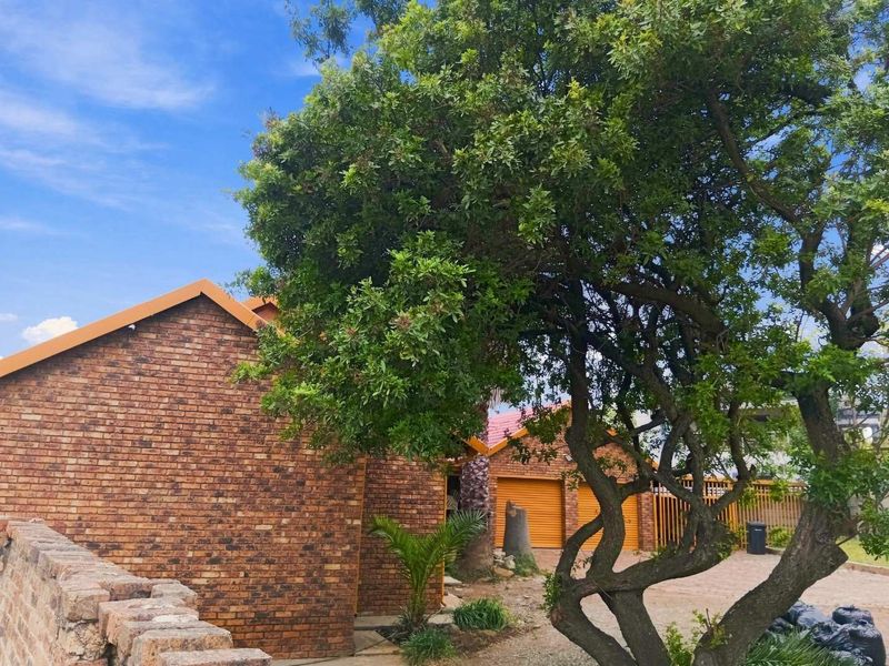 Front exterior view of a face brick house featuring a tiled roof, garage access, and established garden trees.