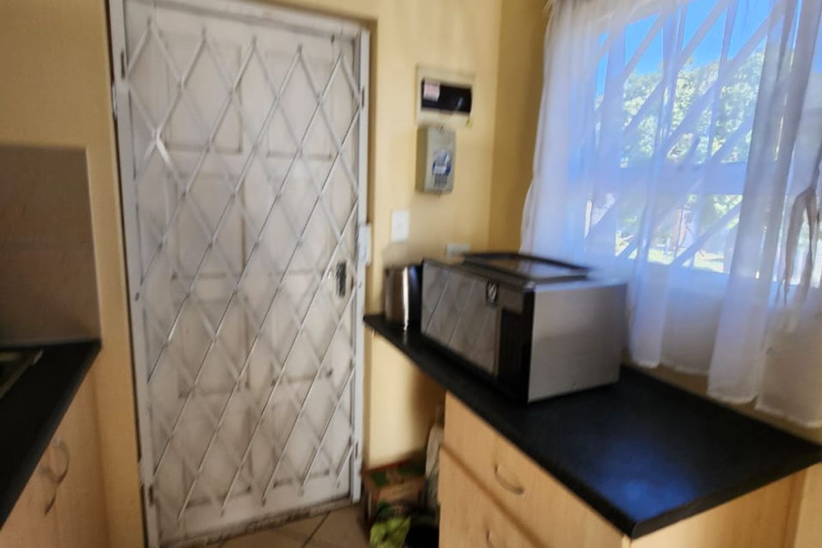 A functional kitchen area featuring built-in cabinetry, dark laminate countertops, tiled flooring, and a security gate leading to the exterior.