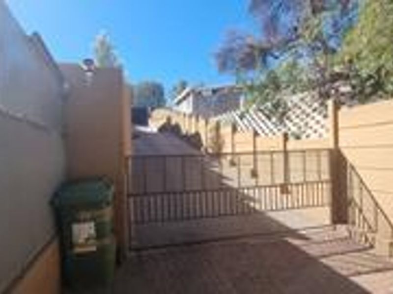 A view of the property entrance featuring a paved driveway, metal security gate, and perimeter boundary walling.