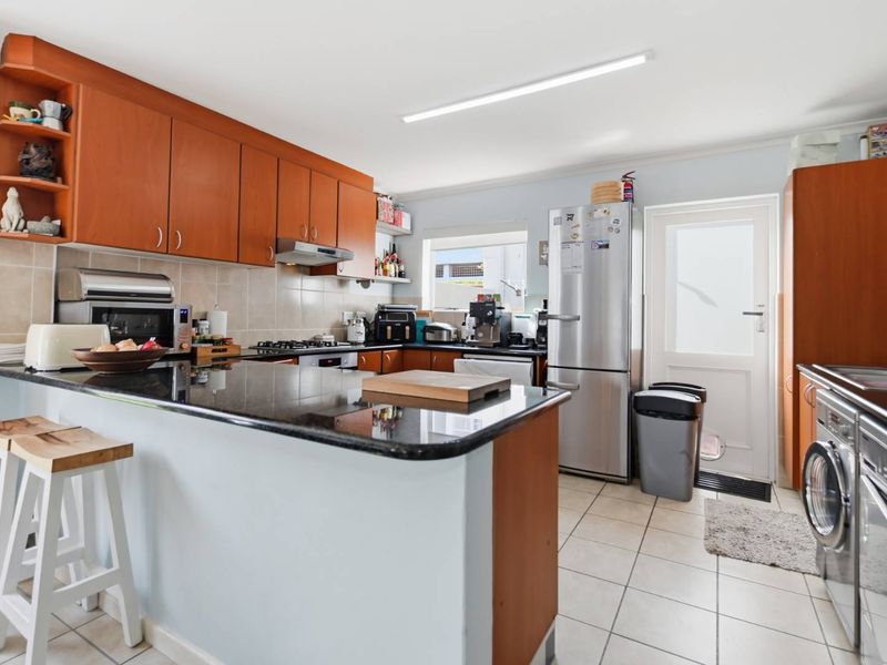 Functional kitchen featuring wooden cabinetry, granite countertops, gas hob, extractor fan, and tiled flooring with direct access to the exterior.