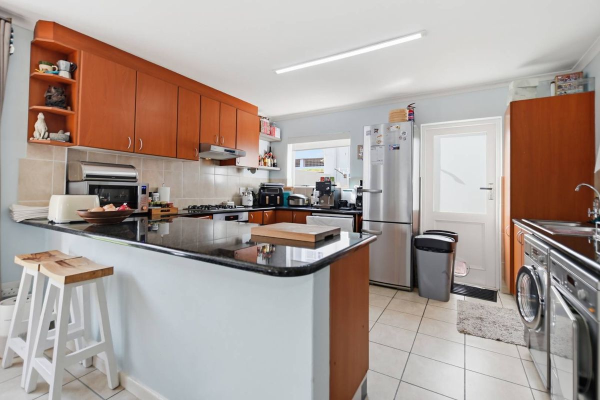 Functional kitchen featuring wooden cabinetry, granite countertops, gas hob, extractor fan, and tiled flooring with direct access to the exterior.