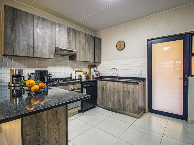 Modern kitchen featuring wood-grain cabinetry, granite countertops, subway tile backsplash, and integrated appliances, leading to an exterior door.