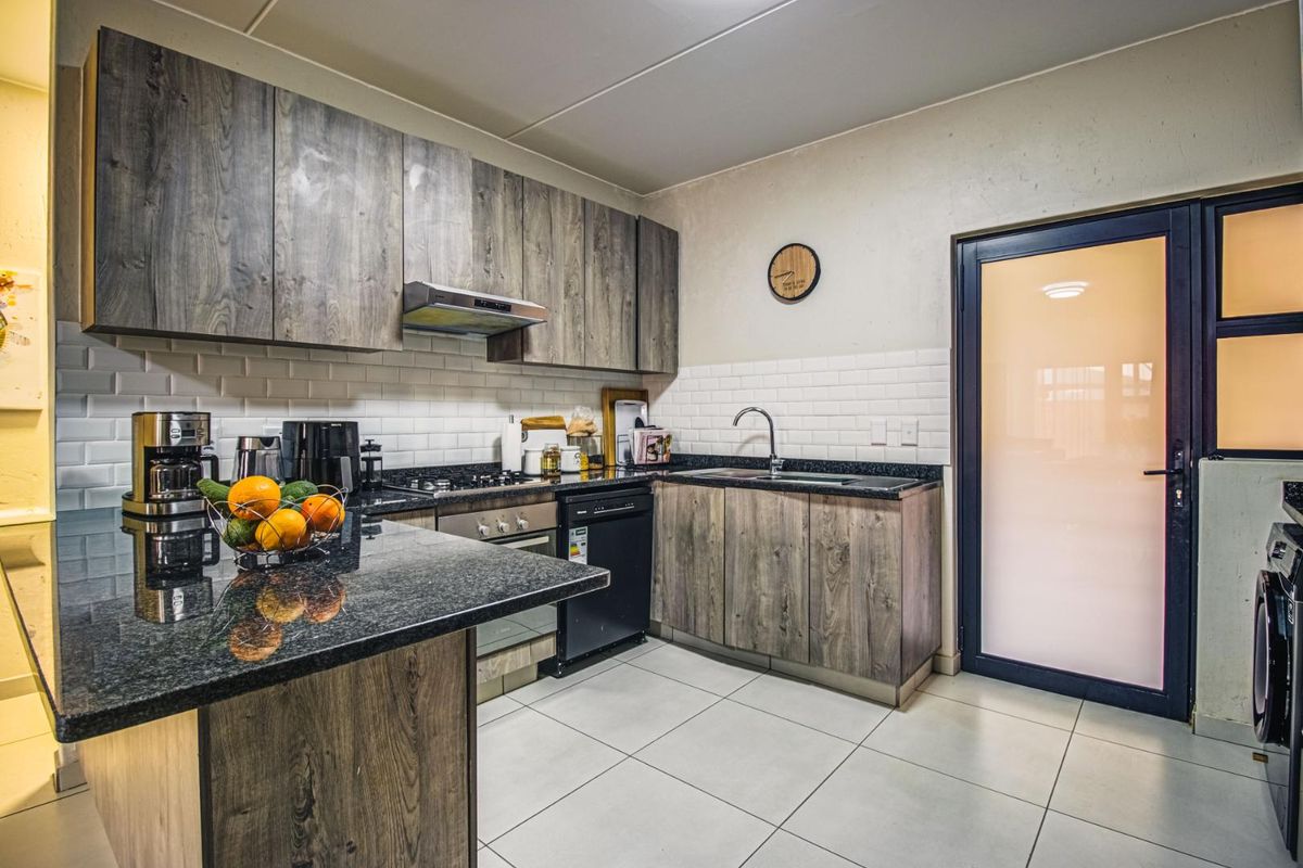 Modern kitchen featuring wood-grain cabinetry, granite countertops, subway tile backsplash, and integrated appliances, leading to an exterior door.