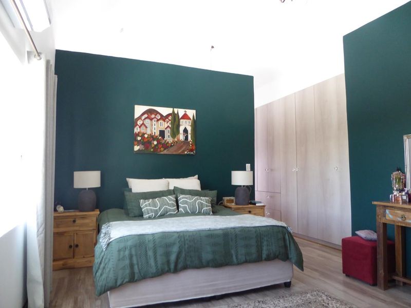 A well-maintained bedroom featuring dark green accent walls, light wood-look laminate flooring, and extensive built-in cupboard storage.