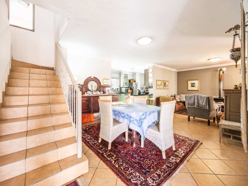 Spacious open-plan living and dining area featuring tiled flooring, a staircase with metal balustrade, and a built-in wood-burning fireplace.