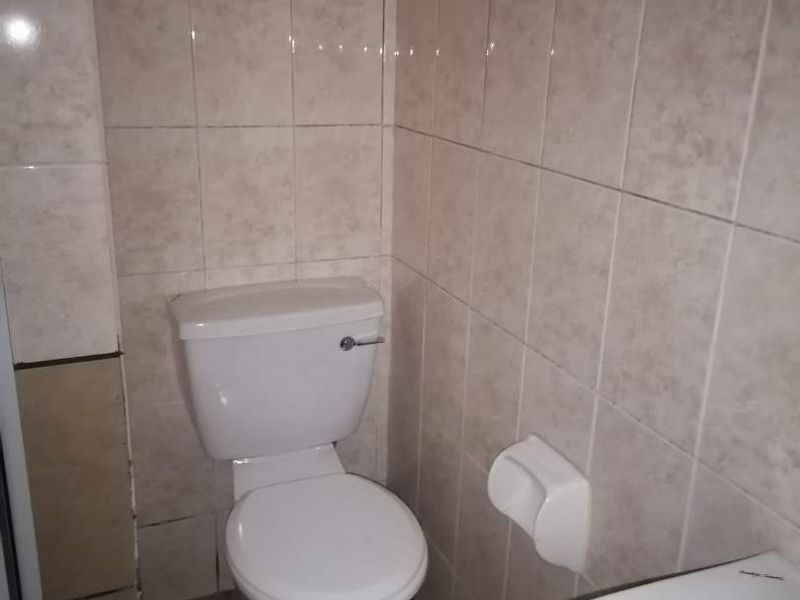 A functional bathroom featuring tiled walls and floors, equipped with a standard toilet and a washbasin.