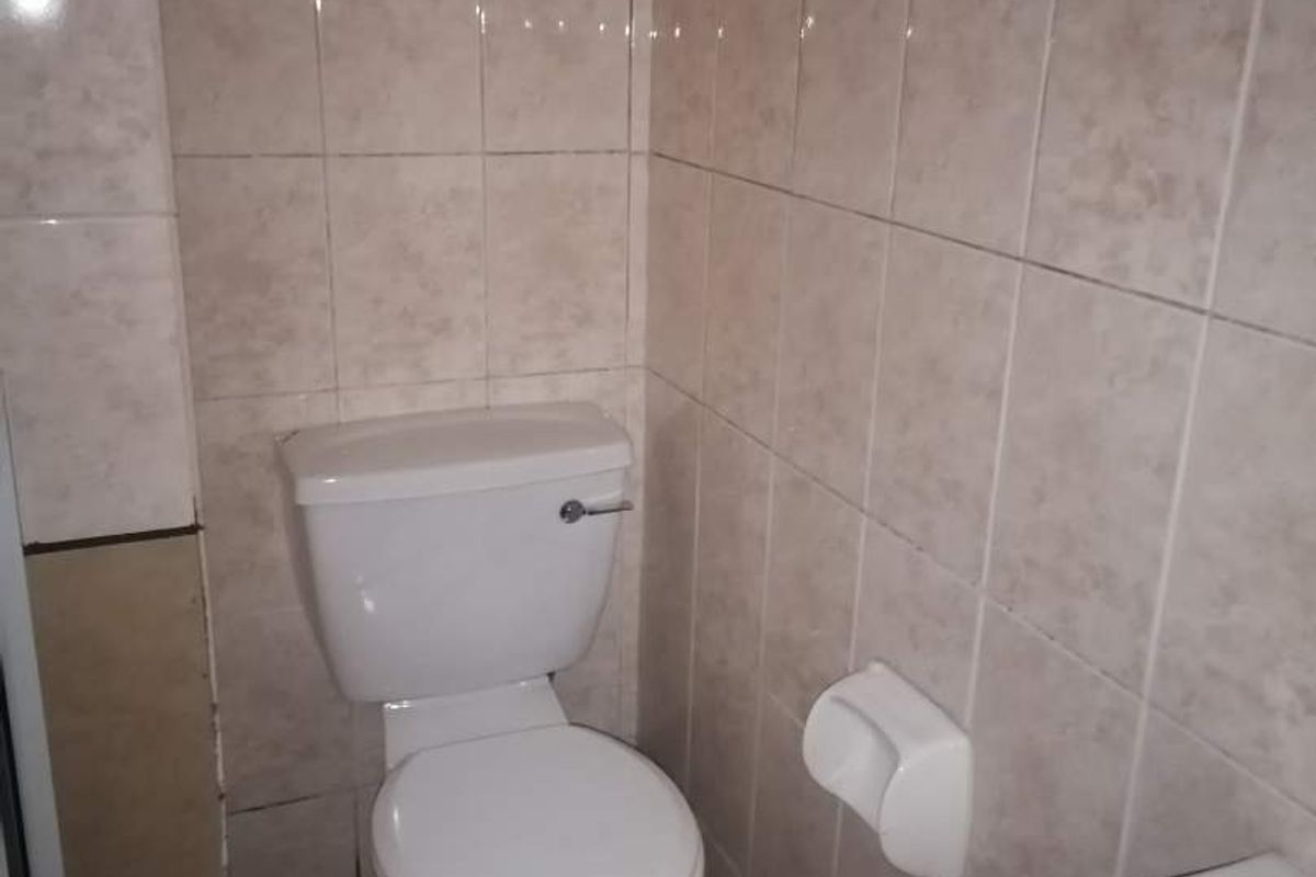 A functional bathroom featuring tiled walls and floors, equipped with a standard toilet and a washbasin.