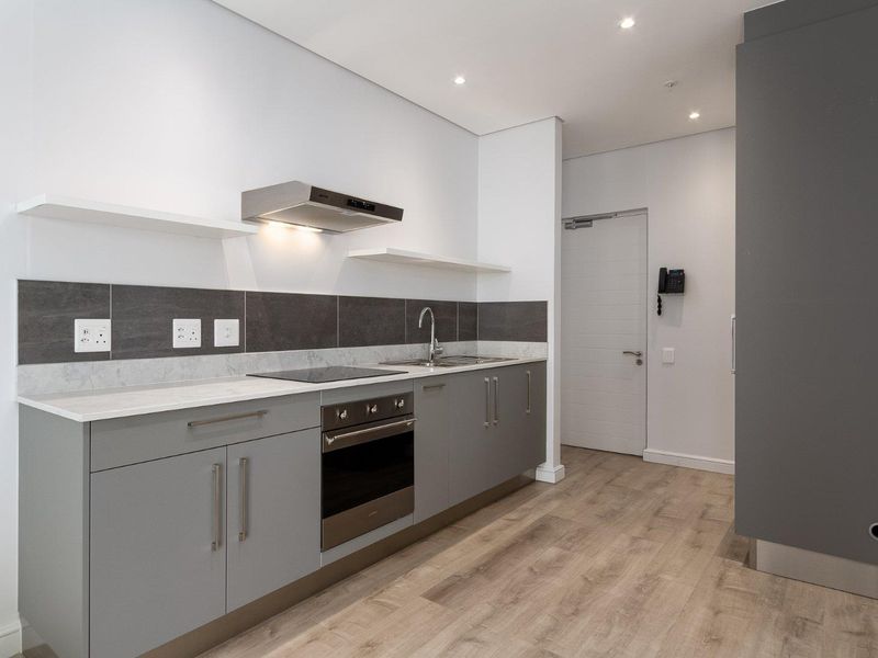 Modern kitchen featuring grey cabinetry, stone countertops, integrated electric oven and hob, stainless steel sink, and contemporary tiled splashback.