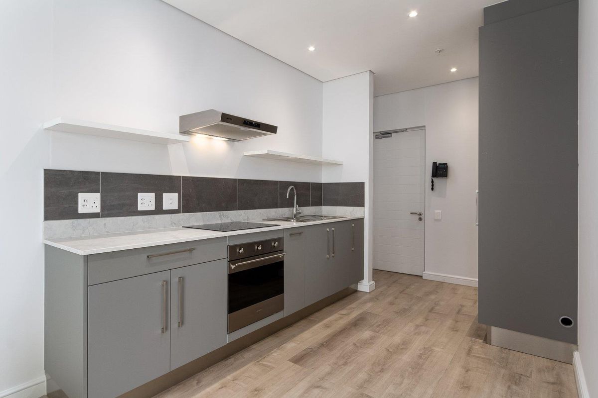Modern kitchen featuring grey cabinetry, stone countertops, integrated electric oven and hob, stainless steel sink, and contemporary tiled splashback.