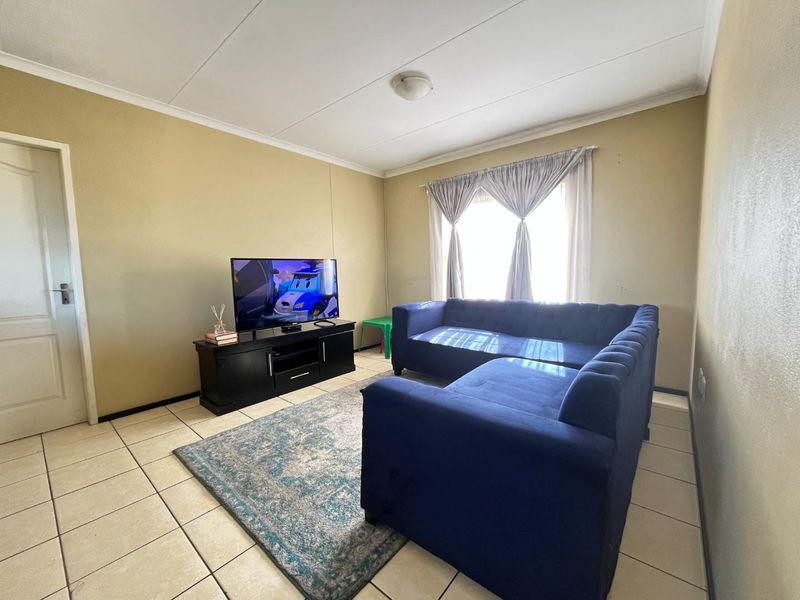 A functional living room featuring neutral wall tones, ceramic floor tiles, and natural light from the window.