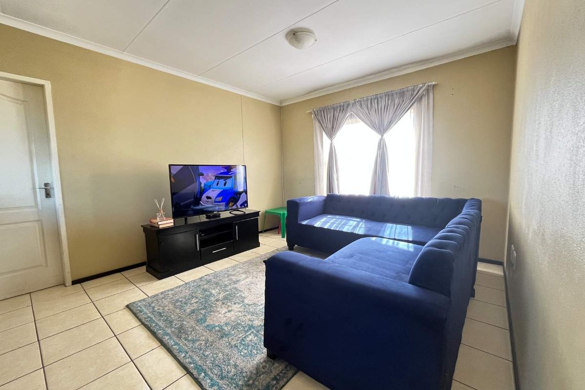 A functional living room featuring neutral wall tones, ceramic floor tiles, and natural light from the window.