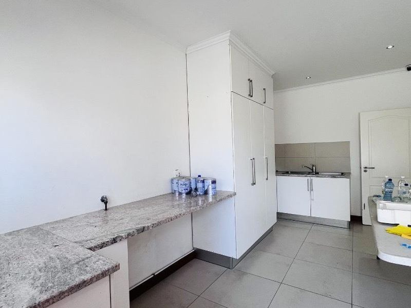 A functional laundry room featuring granite countertops, ample built-in cabinetry, a stainless steel sink, and neutral tiled flooring.