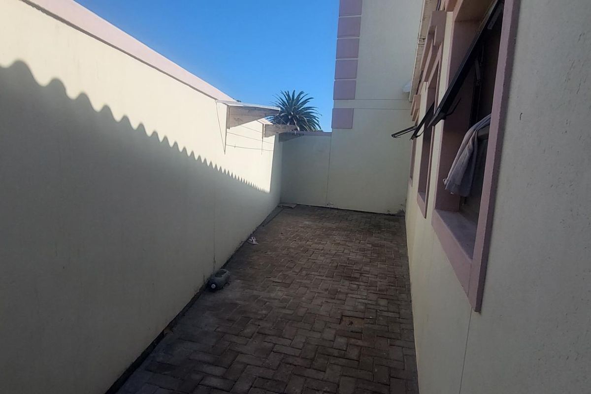 A narrow exterior side passage featuring paved flooring and high boundary walls, providing a functional outdoor utility space.