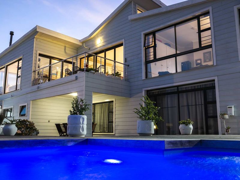 A beautifully presented rear exterior view featuring a modern swimming pool, timber decking, and a spacious balcony with stainless steel balustrades.