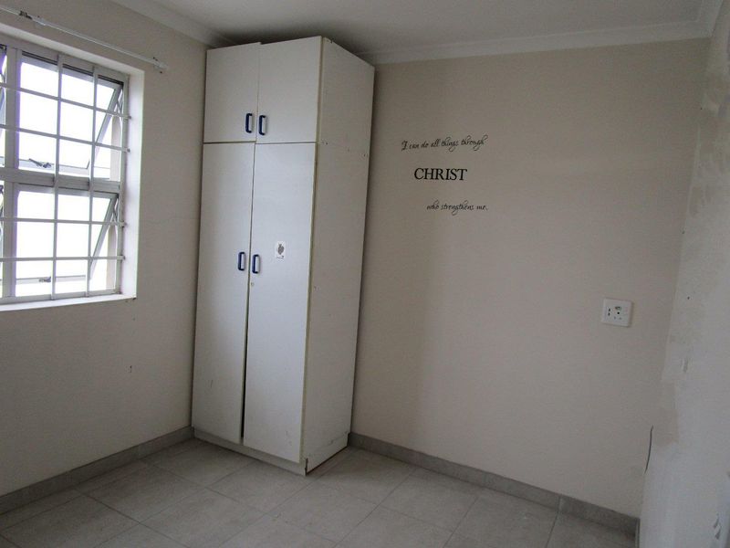 A simple bedroom featuring tiled flooring, a built-in wardrobe, and a window fitted with security bars.