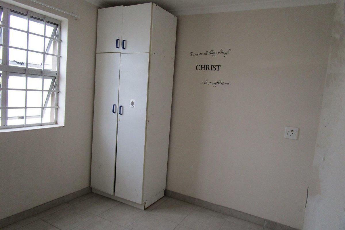 A simple bedroom featuring tiled flooring, a built-in wardrobe, and a window fitted with security bars.