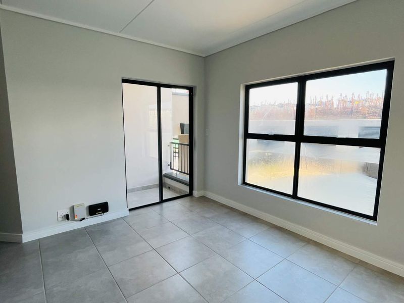 A bright, empty living area featuring modern grey floor tiles, black-framed windows, and a sliding door leading to an outdoor space.