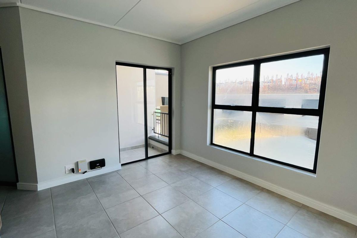 A bright, empty living area featuring modern grey floor tiles, black-framed windows, and a sliding door leading to an outdoor space.