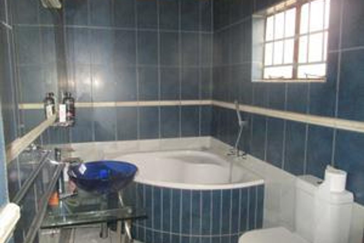 A bathroom featuring a corner bathtub, a glass vessel sink vanity, and blue wall tiling with a window for natural light.