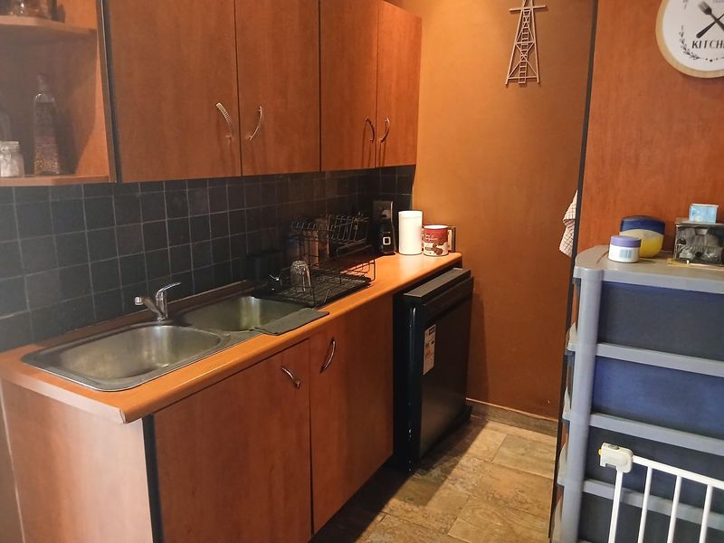 A functional scullery area featuring laminate cabinetry, a stainless steel double sink, and a tiled backsplash, providing additional prep and wash-up space.