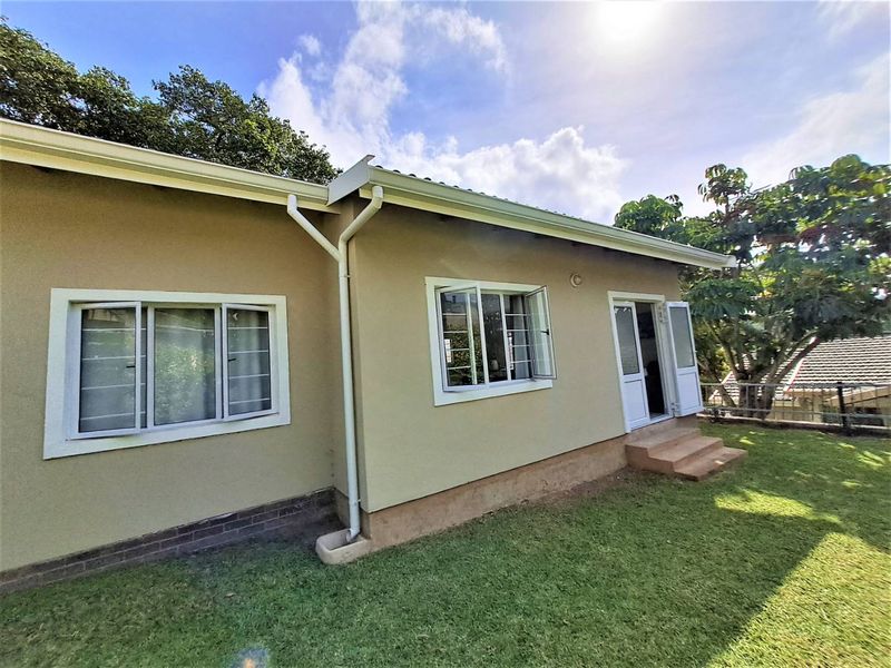 Rear view of the cottage featuring a well-maintained lawn, exterior plaster finish, casement windows with security bars, and access via french doors.