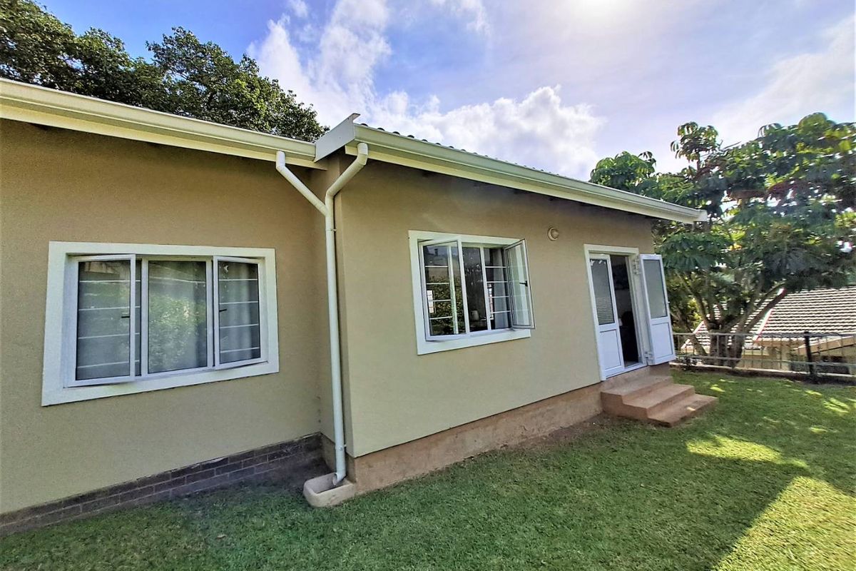 Rear view of the cottage featuring a well-maintained lawn, exterior plaster finish, casement windows with security bars, and access via french doors.