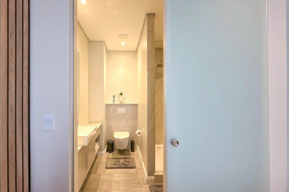 A modern bathroom featuring a wall-mounted toilet, a sleek vanity with a basin, and a walk-in shower, accessed through a frosted glass sliding door.