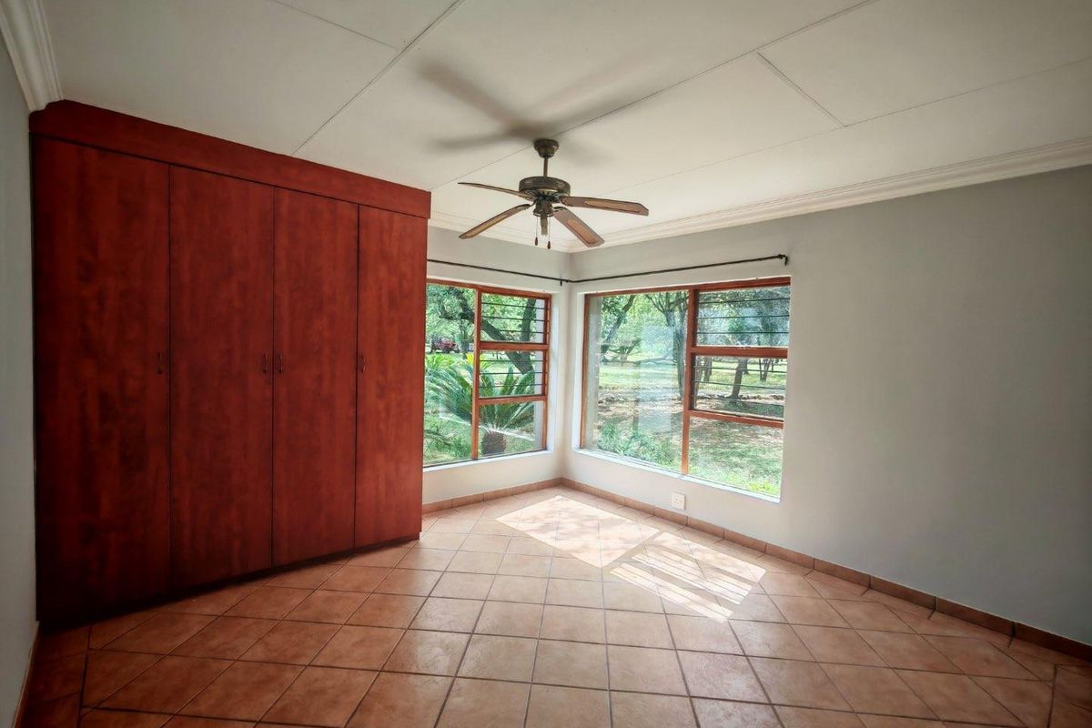 A bright bedroom featuring large windows with garden views, tiled flooring, a ceiling fan, and built-in wooden wardrobes.