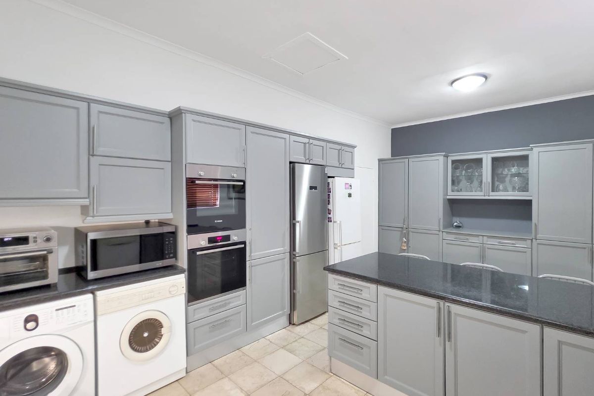 A functional kitchen featuring grey cabinetry, granite countertops, a central island, and integrated appliances, providing ample storage and workspace.