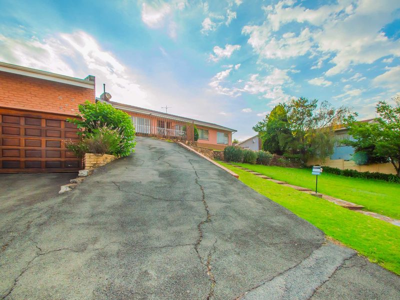 Front exterior view of the property featuring a paved driveway leading to a garage, with a landscaped lawn and retaining wall.