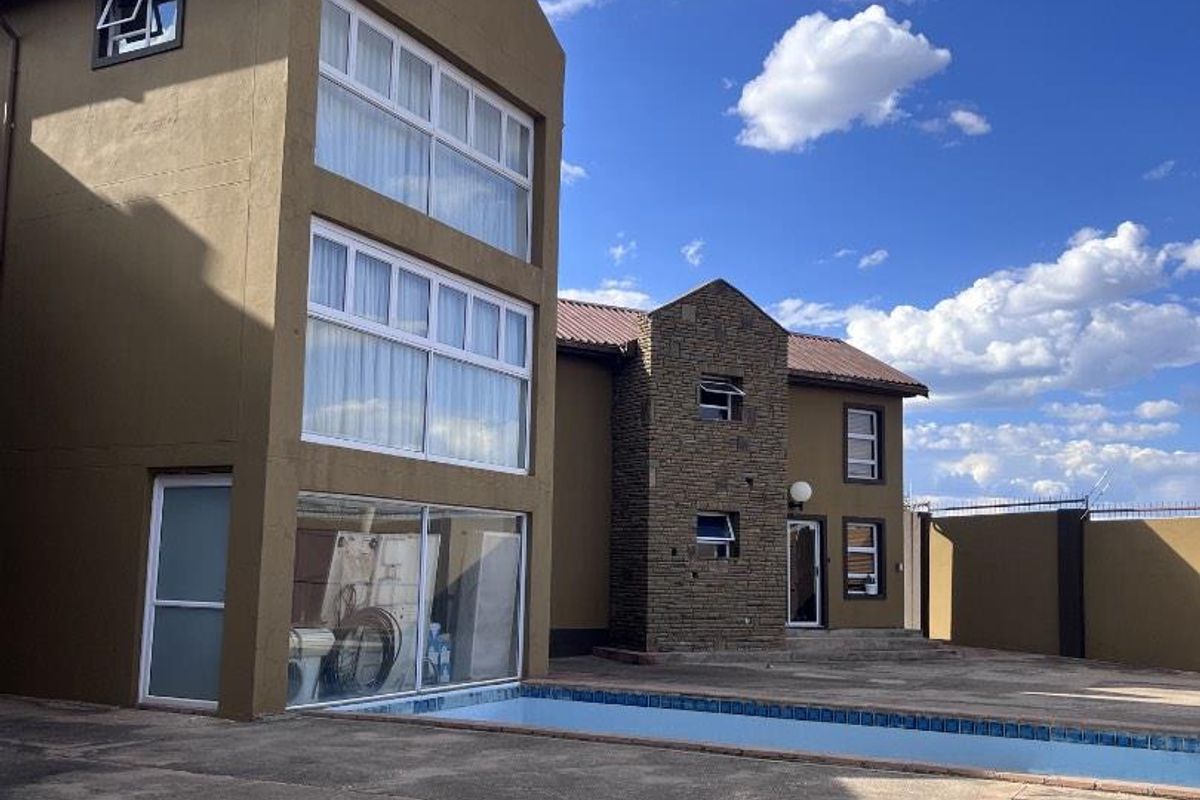 Rear view of a multi-story house featuring a swimming pool, stone-clad facade detail, and large windows overlooking the paved patio area.