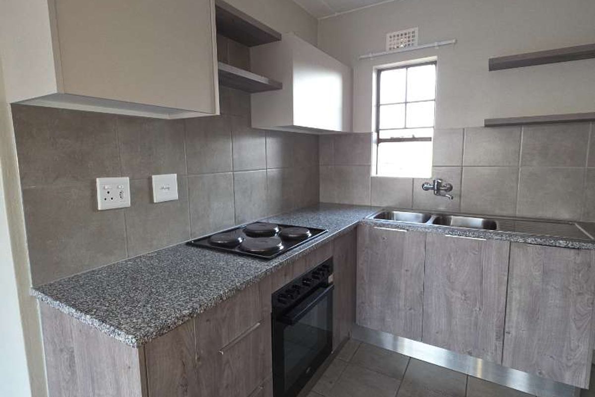 A clean, functional kitchen featuring modern wood-grain cabinetry, granite countertops, a built-in oven and hob, and neutral tiled finishes throughout.