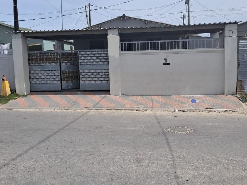 Front exterior view of the property featuring a boundary wall, metal security gate, and paved driveway area.