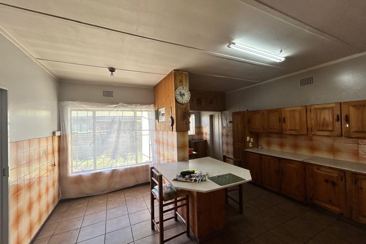 A dated kitchen featuring wooden cabinetry, tiled flooring, and a central breakfast island, offering a functional layout with potential for modernization.