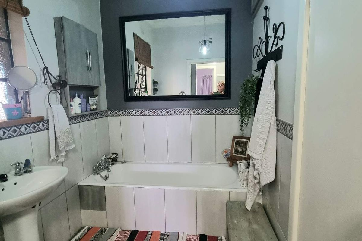 A functional bathroom featuring a pedestal basin, a tiled bathtub with a shower mixer, and decorative border tiling.