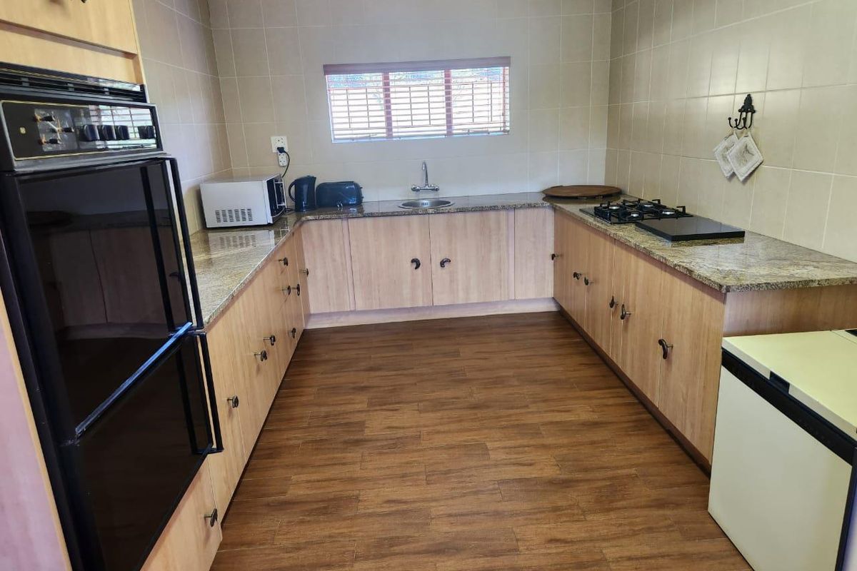 A functional kitchen featuring light wood cabinetry, granite countertops, a built-in oven, and a gas hob, finished with wood-look flooring.