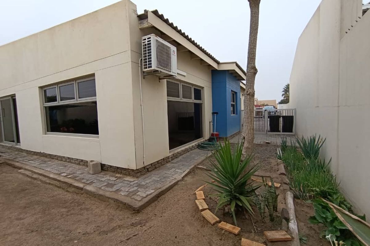 Rear exterior view of the property featuring a paved walkway, boundary wall, and an installed air conditioning unit.