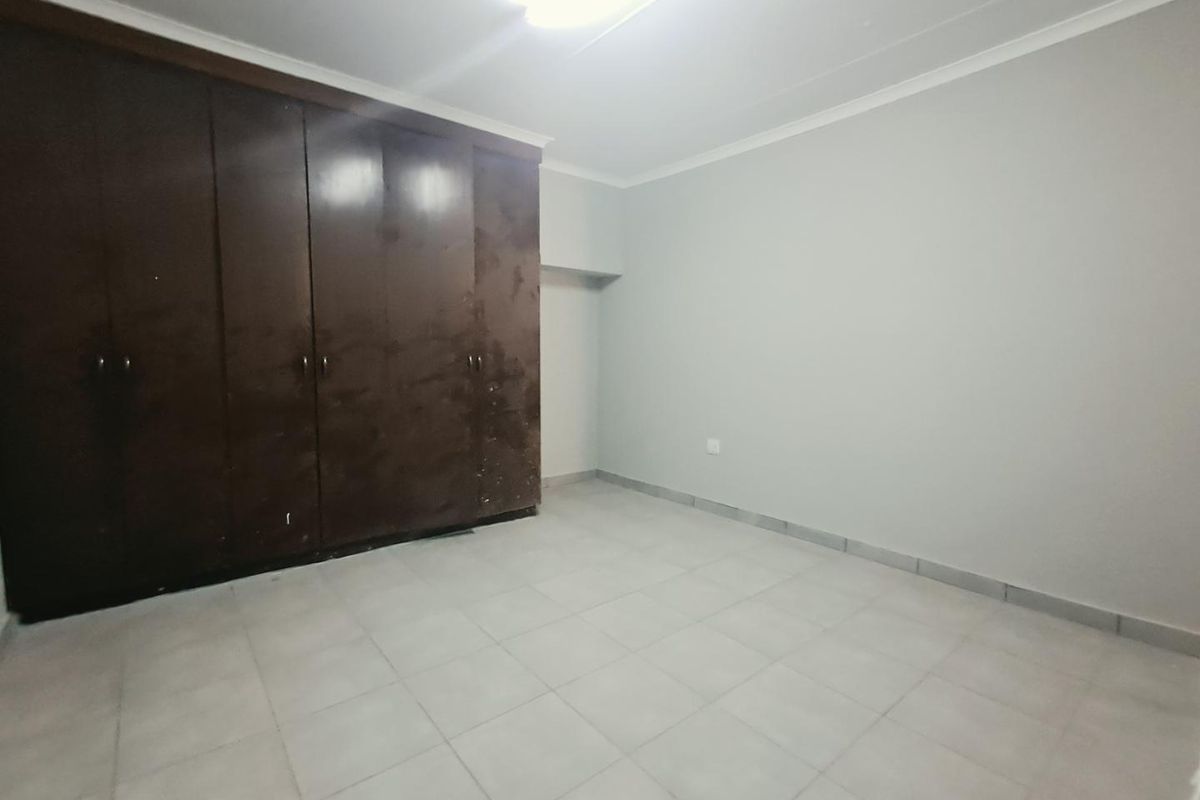 An empty bedroom featuring tiled flooring, coved ceilings, and large built-in cupboards with a dated finish.