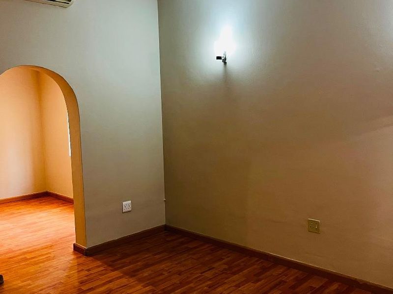 An empty living area featuring warm-toned laminate flooring, a wall-mounted air conditioning unit, and a distinctive architectural archway leading to an adjacent space.