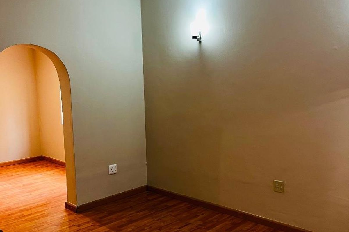 An empty living area featuring warm-toned laminate flooring, a wall-mounted air conditioning unit, and a distinctive architectural archway leading to an adjacent space.