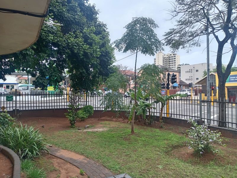 A view of the street frontage featuring a small garden area, metal perimeter fencing, and nearby traffic infrastructure.