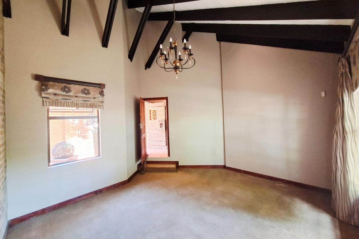 Spacious living room featuring a vaulted ceiling with exposed timber beams, carpeted flooring, and a classic chandelier.